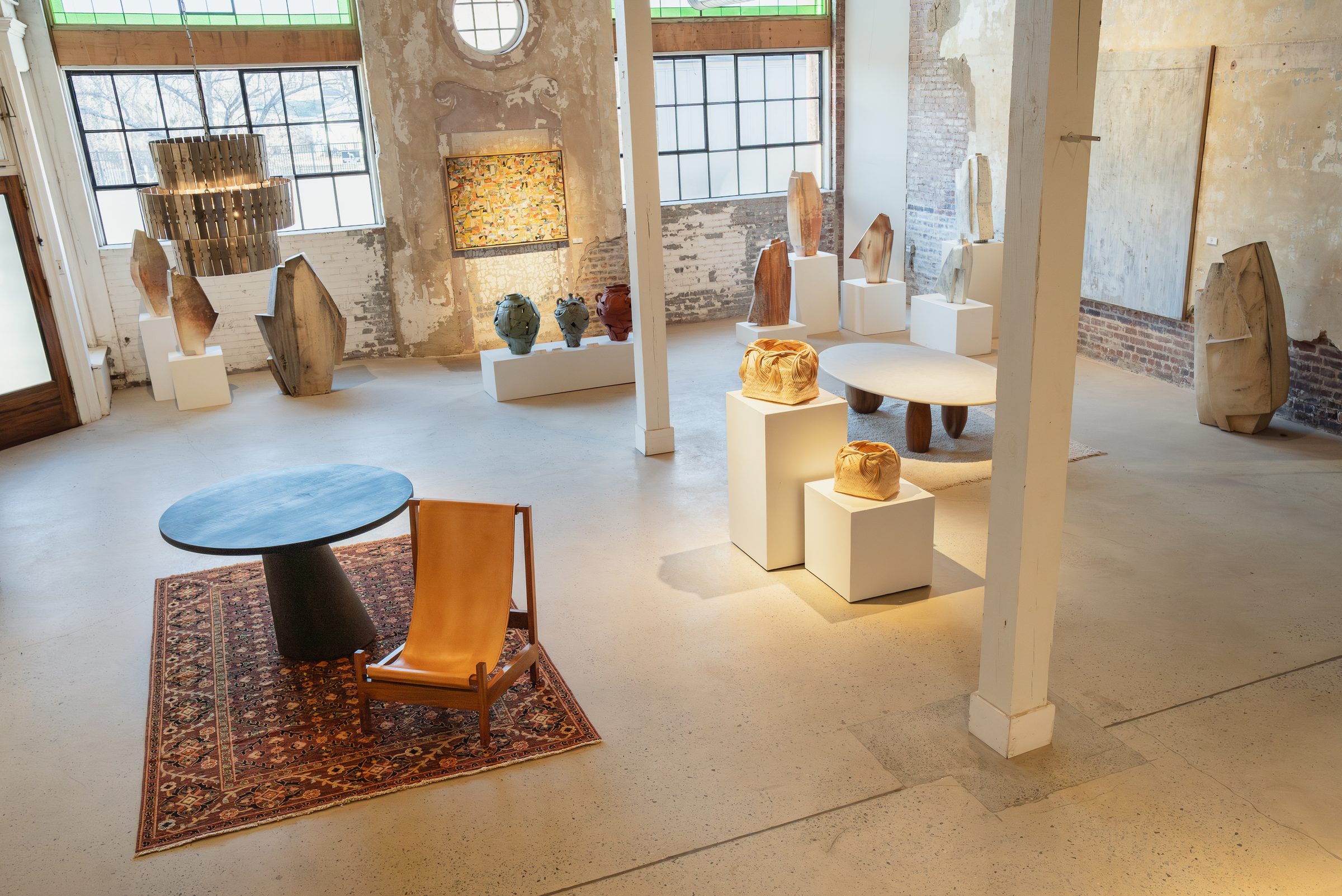 Styled showroom floor with white timber columns, steel-sash windows and a round oculus window, set with furniture and ceramics